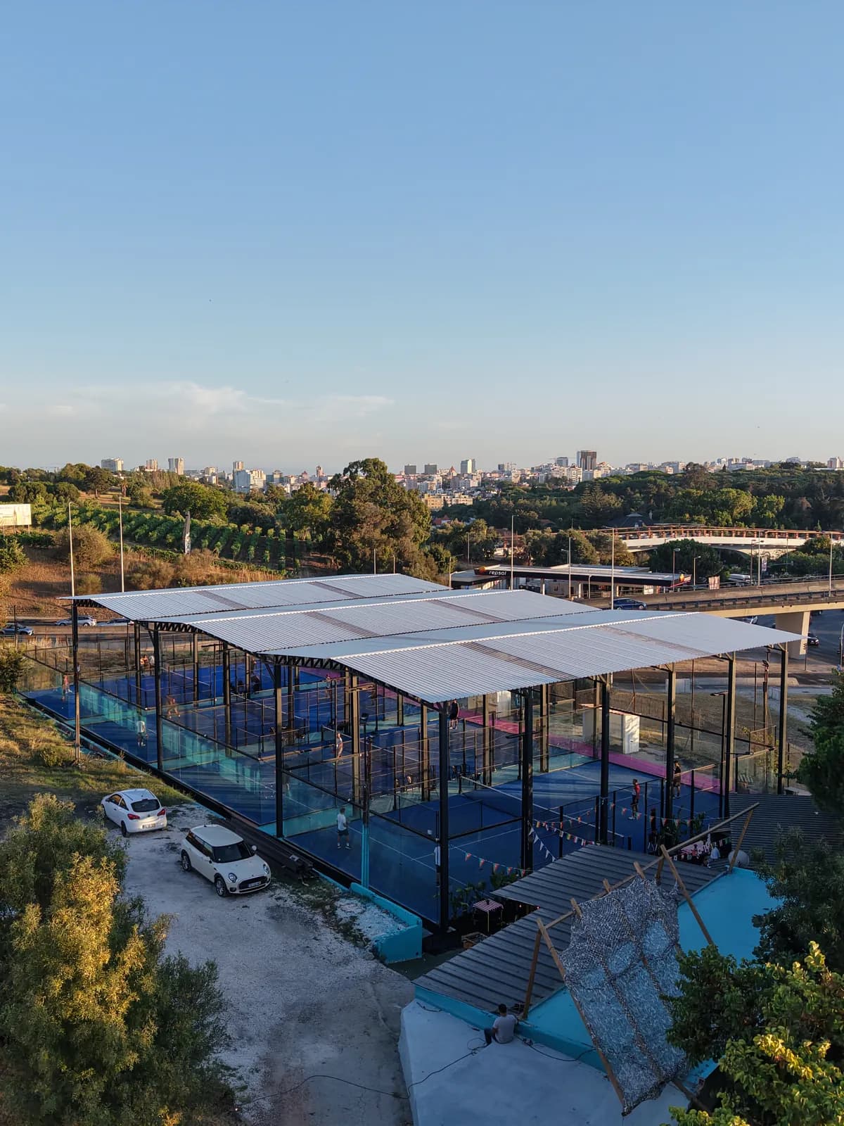 A cobertura branca e os campos envidraçados do clube vistos de perto, com Lisboa ao fundo.
