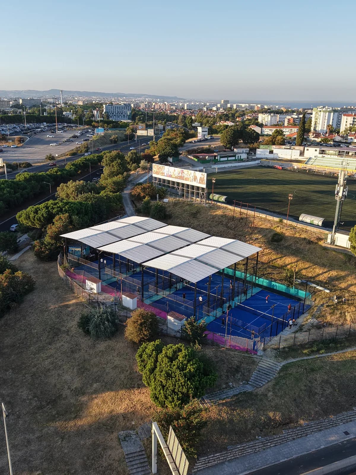 Vista aérea do clube com o campo de futebol vizinho, os bairros de Lisboa e o rio ao fundo.