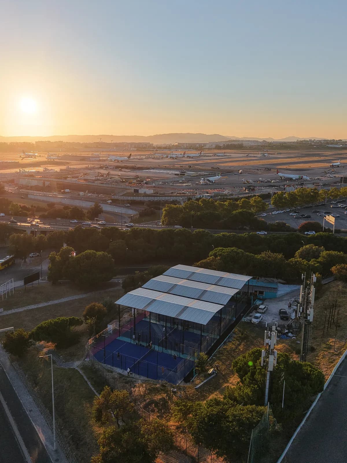 O sol a pôr-se sobre as pistas do aeroporto de Lisboa, com a cobertura e os campos do clube logo abaixo.